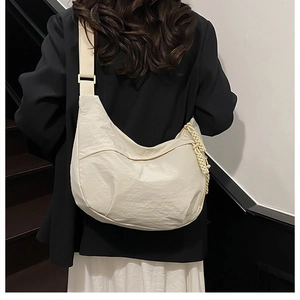 Détail d'un sac demi-lune en nylon crème avec pendentif tressé et large bandoulière