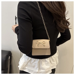 Detail of a chic beige mini crossbody bag featuring a golden metal bow and chain strap
