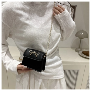 Detail of black leather mini crossbody bag with golden bow hardware and chain strap