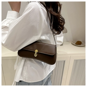 Detail view of a dark brown leather underarm bag with a gold oval metal buckle on a shoulder