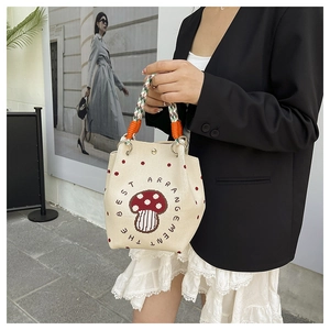 Detail einer beigen Web-Beuteltasche mit Pilz-Stickerei und farbenfrohem Tragegriff
