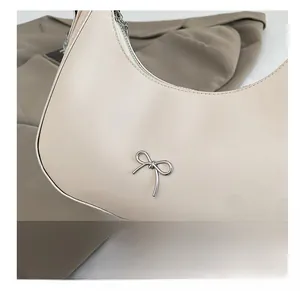 Detail of off-white PU leather crescent bag with silver bow accent and zip closure