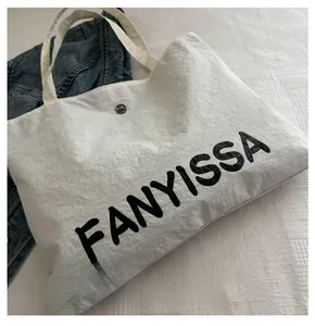 Detail of white canvas tote bag with black FANYISSA lettering and metal logo button