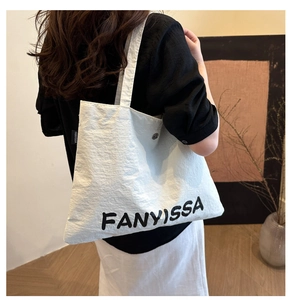 Detailed side view of large white canvas tote bag with black letter print and side label