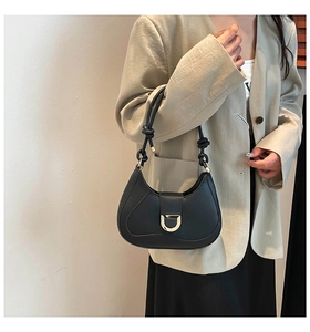 Detail of black leather crescent bag with decorative knotted strap and gold D-shaped buckle