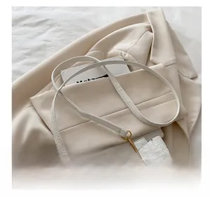 Détail du sac bandoulière en cuir grainé blanc avec boucle dorée sur un blazer