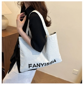 Close-up of white canvas tote bag featuring black FANYISSA logo and side woven label detail