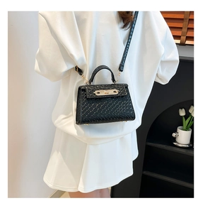 Detail view of black woven texture handbag with golden metal lock and slim shoulder strap