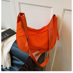 Détail d'un sac bandoulière orange en nylon en forme de demi-lune avec sangle réglable
