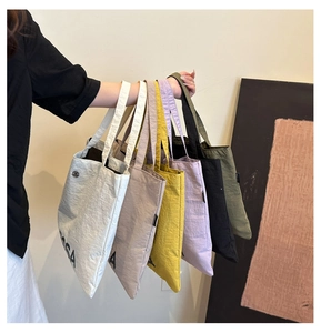 Detail showing various colors of canvas tote bags with black minimalist letter prints