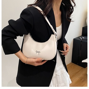 Detail of white half-moon underarm bag featuring a silver bow metal decoration on PU leather