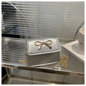 Detail of silver metallic saddle bag featuring a golden bow buckle and fine chain strap