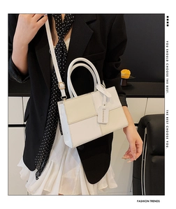 Detail view of stylish white patchwork crossbody bag held by a model in a black blazer