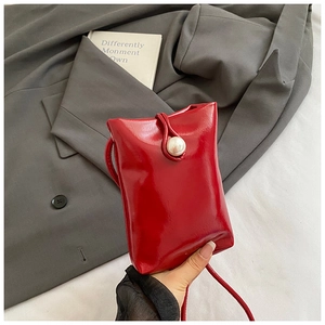 Close-up of a red mini handbag with shiny patent finish and a large pearl buckle