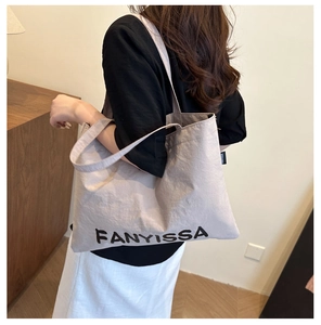 Detailed back view of a person carrying a large beige canvas tote bag with black lettering
