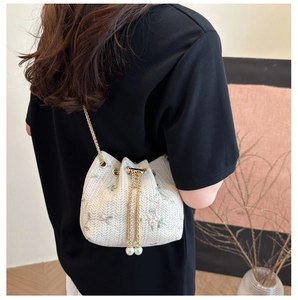 Detail of straw bucket bag with floral embroidery and elegant pearl drawstring tassels