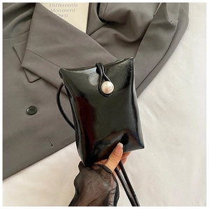 Close-up of black patent leather mini phone bag with large pearl clasp and long strap