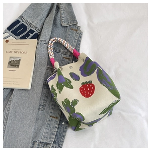 Detail of knitted tote bag with red strawberry pattern and colorful braided handle strap