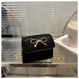 Detail of a black mini saddle bag with a golden bow buckle on a glass shelf