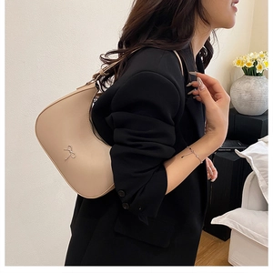 Detail of beige leather crescent hobo bag with a silver bow buckle worn over the shoulder