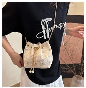 Detail of cream woven bucket bag with floral embroidery and pearl drawstring charm
