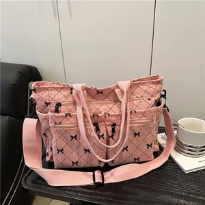 Pink corduroy tote bag with black bow pattern and adjustable strap on a cozy desk setting
