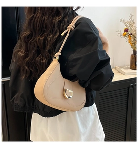 Detail of beige crescent underarm bag with gold D-buckle and stitching on shoulder strap