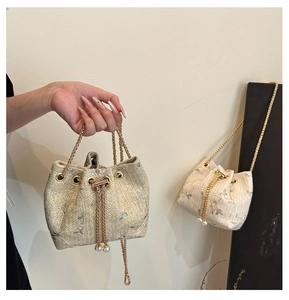 Detail view of woven bucket bag with floral embroidery and gold pearl chain strap