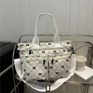 White corduroy tote bag with black bow lattice pattern and multiple zipper pockets
