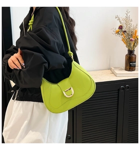 Detail of lime green underarm bag with gold D-buckle shown on shoulder in a stylish home setting
