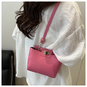 Détail d'un sac bandoulière rose motif litchi avec fermoir rotatif doré et bandoulière en cuir