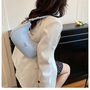 Detail view of light blue crescent shoulder bag with silver bow hardware on a model