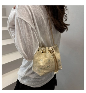 Close-up of beige straw bucket bag with floral embroidery and pearl drawstring detail