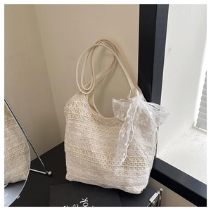 Gros plan d'un sac à bandoulière en dentelle beige avec motifs floraux et grand nœud décoratif