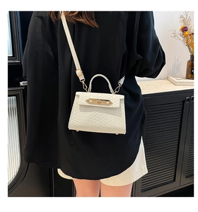 Close-up of white mini handbag with woven texture and gold clasp on a crossbody strap