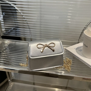 Chic silver mini bow crossbody bag with golden chain strap on stylish glass display