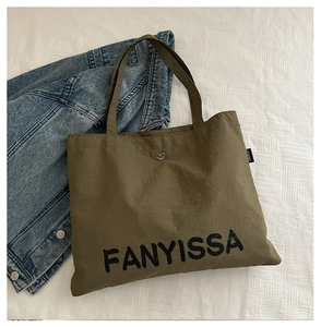 Detail of army green canvas tote bag with black FANYISSA logo and metallic button closure