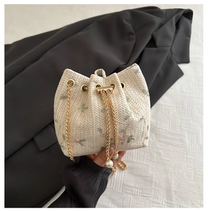 Detail of floral embroidery, gold chain strap, and pearl accents on a beige straw bucket bag