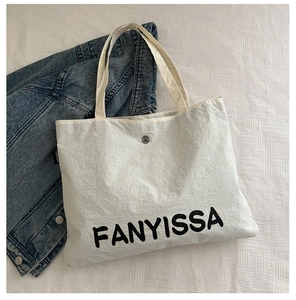 Detail of silver magnetic buckle and FANYISSA logo on white canvas tote bag texture