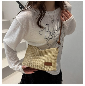 Detail of hand-woven straw tote with brown leather logo patch and slim shoulder straps