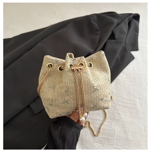 Detail of floral embroidery on a beige straw bucket bag with gold chain strap