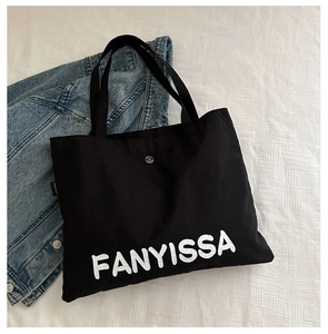 Flat lay view of a large black canvas tote bag with FANYISSA lettering and denim jacket
