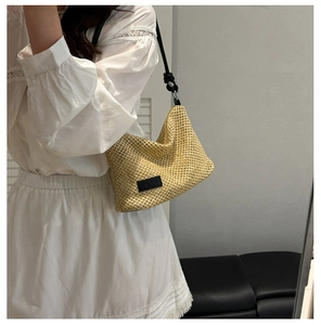 Detail of beige woven straw tote bag with black strap and textured grid pattern