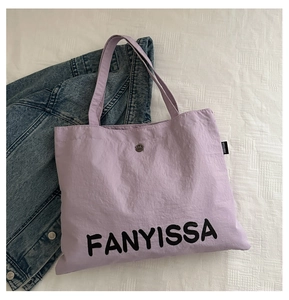 Detailed close-up of purple canvas tote bag with metal snap closure and brand logo