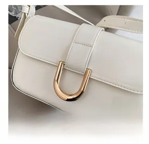Close-up of a cream-colored baguette bag featuring a gold U-shaped metal buckle detail