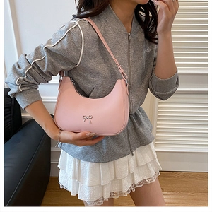 Pink hobo shoulder bag with silver bow ornament shown on model in a home setting