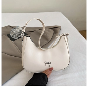 Macro shot of cream-white hobo bag with a silver bow detail and polished faux leather