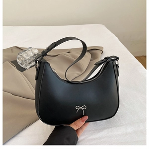 Detail of black crescent bag featuring a silver metal bow and adjustable strap