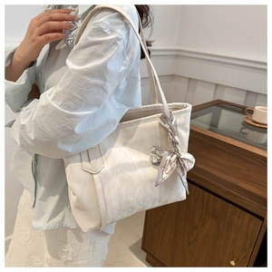 Detail of cream tote bag featuring a decorative fashion ribbon and slim shoulder strap