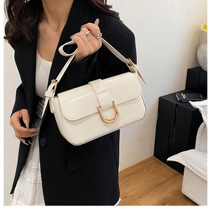 Detail of cream white patent leather handbag featuring a golden horseshoe metal buckle